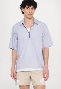 Camicia a maniche corte a righe azzurre chiare con colletto a zip, due tasche frontali e bordi in pizzo bianco all'orlo.