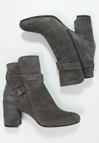 Paar graue Wildleder-Ankle-Boots mit Blockabsätzen, seitlichem Reißverschluss und dekorativem Riemen mit silberner Schnalle an jedem Stiefel.