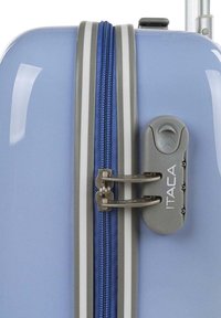 Maleta azul de concha dura con un zipper plateado y un candado de combinación. Textura suave con un brillo metálico. Acentuada con herrajes grises.
