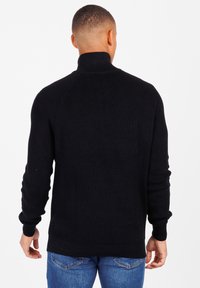 Schwarzer, gerippter Rollkragenpullover mit langen Ärmeln, taillierter Passform und hohem Kragen. Kombiniert mit blauen Jeans aus Denim, die eine glatte Textur aufweisen.