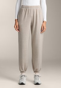 Lichtbeige sweats in een zachte stof, met een elastische tailleband en omgeslagen boorden. Gecombineerd met grijze sportschoenen.