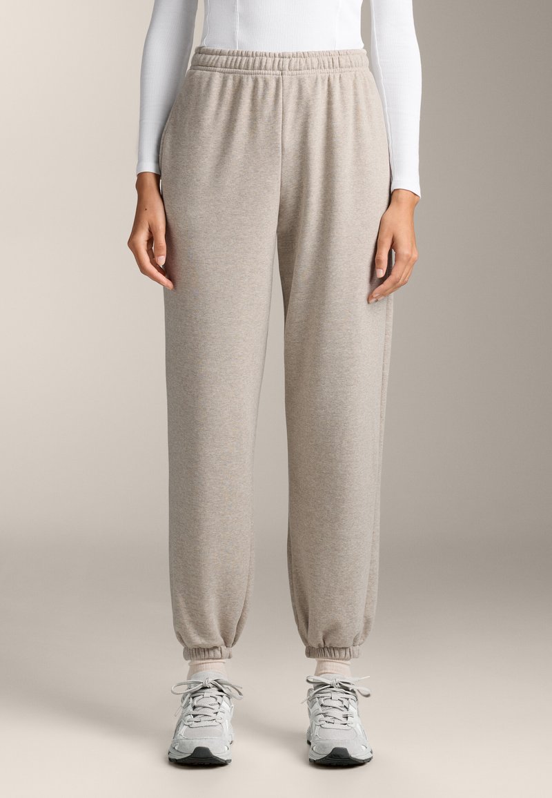 Lichtbeige sweats in een zachte stof, met een elastische tailleband en omgeslagen boorden. Gecombineerd met grijze sportschoenen.