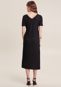 Schwarzes Midi-Kleid aus strukturiertem Stoff, mit V-Ausschnitt und kurzen Ärmeln. Hat eine gerade Silhouette und wird mit schwarzen Riemchenschuhen kombiniert.
