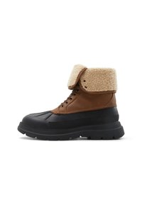 Botas de invierno de cuero marrón y goma negra con un puño de borreguillo, punta redonda, cintas y suela texturizada. Presenta costuras y ojales.