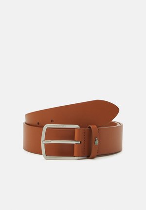 Ceinture en cuir marron roulée avec boucle rectangulaire en argent et petit logo crocodile vert sur la boucle de ceinture, sur fond blanc.