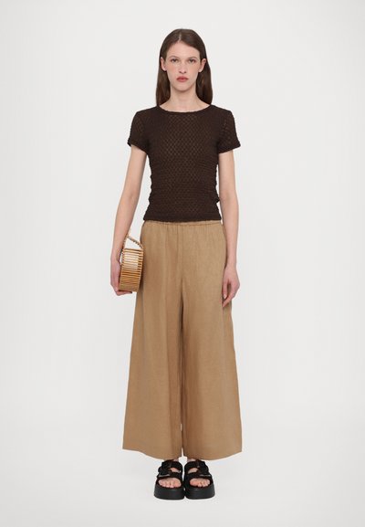 Brązowa, fakturowana bluzka z krótkim rękawem zestawiona z beżowymi spodniami o szerokich nogawkach i masywnymi czarnymi sandałami. Akcesorium: paskowa drewniana kopertówka.