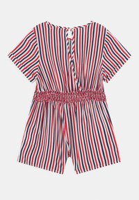Romper w paski charakteryzuje się czerwono-białymi i granatowymi pionowymi paskami, krótkimi rękawami, marszczonym pasem w talii oraz zapięciem na guziki z tyłu.