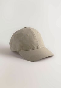 Beige hattu, jossa on pyöreä kruunu, kuusi tuuletusaukkoa ja kaareva lippa. Valmistettu teksturoidusta kankaasta, jossa on näkyvät ommeltyylit.