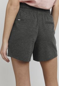 Šedé sportovní šortky vyrobené z měkké látky, s elastickým pasem a dvěma zadními kapsami. Minimalistický design bez vzorů nebo ozdob.