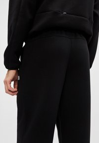 Czarne dresy wykonane z miękkiego, teksturowanego materiału. Posiadają dopasowaną talię i boczne szwy z subtelnym logo blisko dołu.