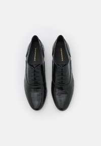 Chaussures en cuir noir texturé avec un motif crocodile, dotées de lacets et d'un design à bout rond. Nom de la marque en or à l'intérieur.
