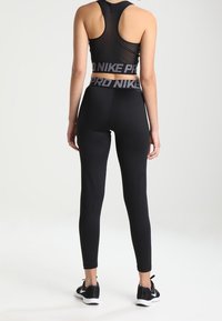 Tenue de sport noire comprenant un soutien-gorge de sport ajusté sans manches avec un dos en mesh et un legging taille haute. Les deux pièces sont en tissu extensible.