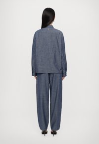 Temna modra denim srajca in široke hlače. Tkanina ima subtilno teksturo, ovratnik in zapenjanje na manšeti.