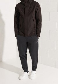 Czarna wodoodporna kurtka z kapturem, kieszenie na zamek. Szare dresy z elastycznymi ściągaczami oraz białe trampki o prostym designie bez widocznych logo.