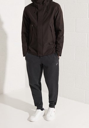 Czarna wodoodporna kurtka z kapturem, kieszenie na zamek. Szare dresy z elastycznymi ściągaczami oraz białe trampki o prostym designie bez widocznych logo.