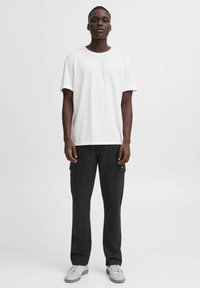 Vit kortärmad T-shirt kombinerad med svarta cargobyxor med sidofickor, bärs med grå sneakers. Enkel och avslappnad passform.