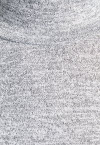 Gros plan d’un tissu tricoté gris clair avec des coutures visibles et une texture douce.