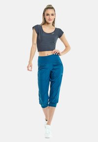 Sivi crop top s kratkim rukavima i plave hlače do tri četvrtine s džepovima i suženim krojem. Glatka tkanina s blagim sjajem.