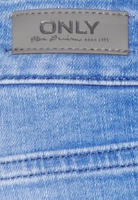 Étiquette en denim de ONLY, présentant un tissu bleu clair, des accents cousus et un patch rectangulaire gris avec du texte en relief.