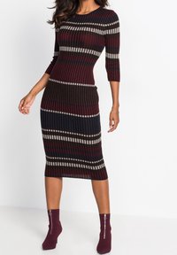 Robe midi en tricot à manches trois-quarts, présentant des rayures horizontales bordeaux, noires et grises. Associée à des bottines ajustées bordeaux.