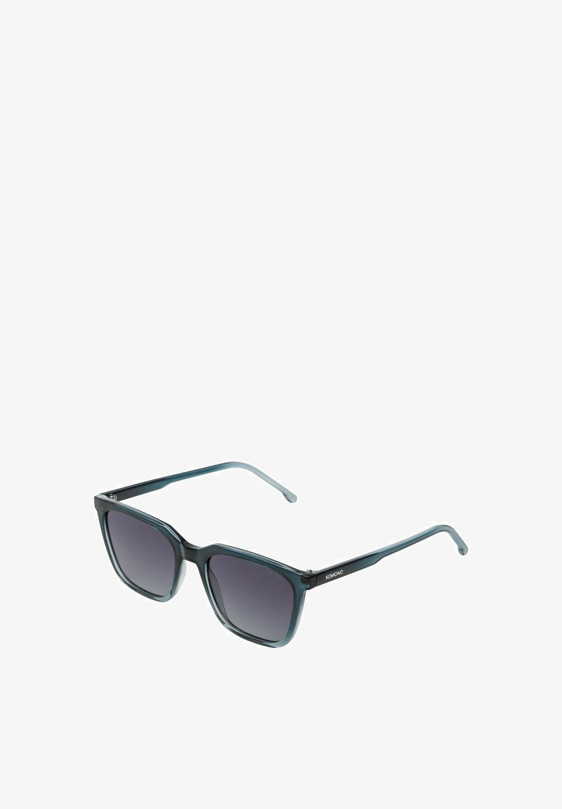 Lunettes de soleil carrées avec une monture en plastique teal foncé et des verres gris dégradés. Les branches fines présentent un détail de logo. Texture lisse sur l'ensemble.