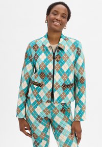 Gekürzte Jacke in Blau, Braun und Weiß mit Rautenmuster und Leopardenakzenten. Sie hat einen Frontreißverschluss, einen Kragen und zwei Seitentaschen.