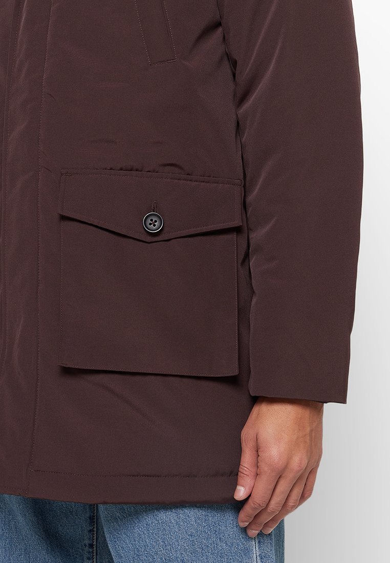 Bruine gevoerde jas met een gladde textuur, voorzien van een knoopzak op de borst en een normale fit. De mouw toont stiksels en heeft een zachte afwerking.