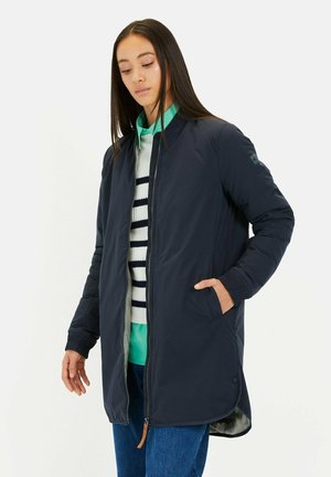 Marineblauwe lichtgewicht jas met een rits, gestructureerde pasvorm, geribbelde manchetten en zijzakken; gelaagd over een gestreepte trui en een groene shirt.