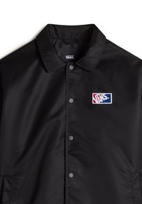 Veste noire Vans avec col, boutons-pression sur le devant et un petit patch du logo Vans rouge, blanc et bleu sur la poitrine.