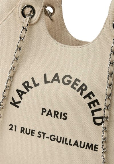 Бежова платнена чанта с сребристи верижни дръжки и черен текст „KARL LAGERFELD PARIS 21 RUE ST-GUILLAUME“ отпред.