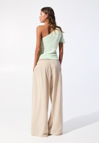Groene top met één schouder en korte mouwen, gecombineerd met brede, beige broek. Zachte stof met een relaxed, vloeiend figuur.