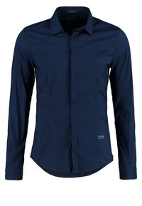 Męska granatowa slim-fit koszula z długim rękawem, z krytą listwą guzików i małym logo "GUESS Los Angeles" blisko dolnego końca.