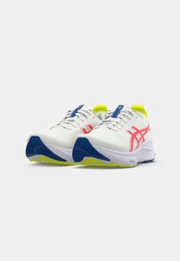 White athletic shoes with pink accents, blue detailing, and a neon yellow heel. Textured upper and contrasting rubber sole for traction.