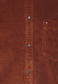 Hnědá kordová košile s button-up designem, stříbrnými knoflíky a kapsou s malou logomerkou na boku.