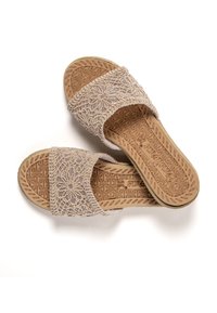 Sandalias beige de tipo slip-on con un patrón floral de encaje en la correa y suelas de goma con diseño. Parte superior texturizada y plantilla contorneada.
