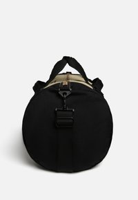 Borsa rotonda nera realizzata in tessuto resistente. Presenta una maniglia superiore robusta e una tracolla nera con un gancio in plastica. Accent in marrone sulla zona della zip.