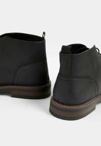 Černé kožené kotníkové boty s hladkým povrchem, táhlem na patě a akcentem z hnědého dřevěného podpatku. Minimalistický design s kulatou špičkou.