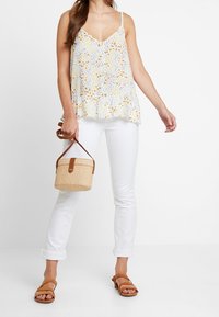 Canotta floreale con motivi gialli e blu, scollo a V, orlo svasato; abbinata a jeans bianchi arrotolati e sandali marroni, mentre tiene una borsa rotonda di paglia.