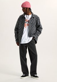 Chaqueta de franela a cuadros en negro y gris, camiseta gráfica blanca, pantalones grises y zapatos negros con acentos blancos. Gorro de lana de color rosa.