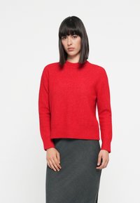 Red knit sweater with a crew neck, long sleeves, and a cropped hem. The texture appears soft, with a smooth finish. Paired with a dark gray skirt.