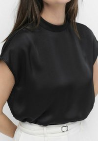 Sort satin top med høj hals, korte kapærmer og en glat, blank tekstur. Kombineret med lystfarvede strukturerede bukser.