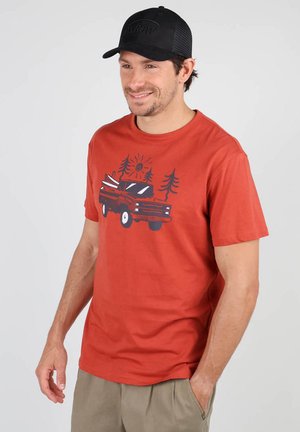 T-shirt en coton rouge à col ras du cou avec un graphisme d'un camion portant des planches de surf, des pins et un soleil. Associé à une casquette de baseball noire.