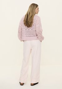 Light pink knitted sweater with a geometric openwork pattern, paired with loose-fitting light pink trousers. Flat sandals complete the look.