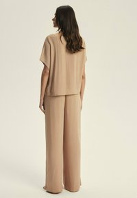 Beige, loose-fitting top with short sleeves paired with wide-leg trousers. Smooth fabric with a soft texture, no visible patterns or hardware.