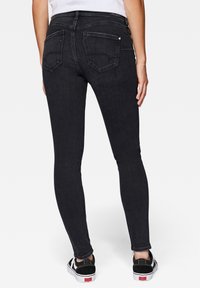 Jeans ajustados negros con una textura suave, que cuentan con dos bolsillos traseros y una cintura de altura media, combinados con zapatillas negras con suelas blancas.