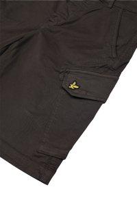 Pantaloni cargo in tessuto marrone scuro, con tasche laterali e un logo ricamato giallo sulla tasca sinistra. Superficie strutturata, vestibilità casual.