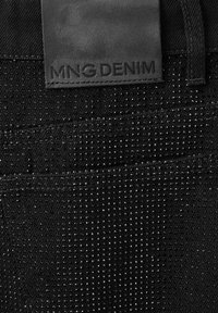 Tissu en denim noir avec de petites clous brillants et une étiquette en cuir noir embossée avec "MNG DENIM" au-dessus d'une passante de ceinture.