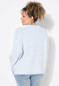 Maglione azzurro chiaro a coste realizzato in morbido materiale, con scollatura rotonda e spacchi laterali, abbinato a jeans blu sbiaditi.