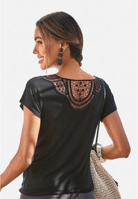 Schwarzes T-Shirt mit kurzen Ärmeln und einem Häkelmuster am Rückenausschnitt. Glattes Material, runder Ausschnitt, kombiniert mit einer geflochtenen Tasche.
