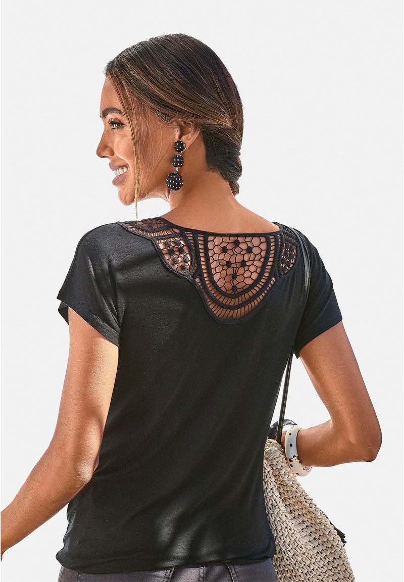Schwarzes T-Shirt mit kurzen Ärmeln und einem Häkelmuster am Rückenausschnitt. Glattes Material, runder Ausschnitt, kombiniert mit einer geflochtenen Tasche.